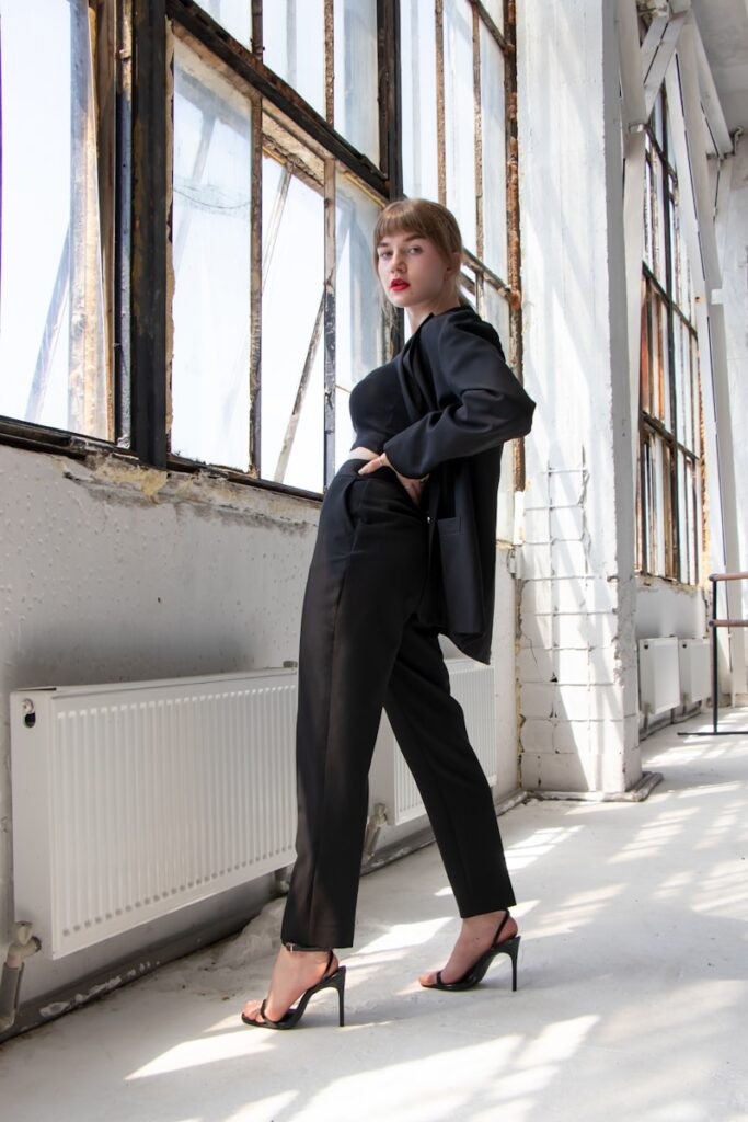 woman in black blazer and gray pants standing beside window during daytime