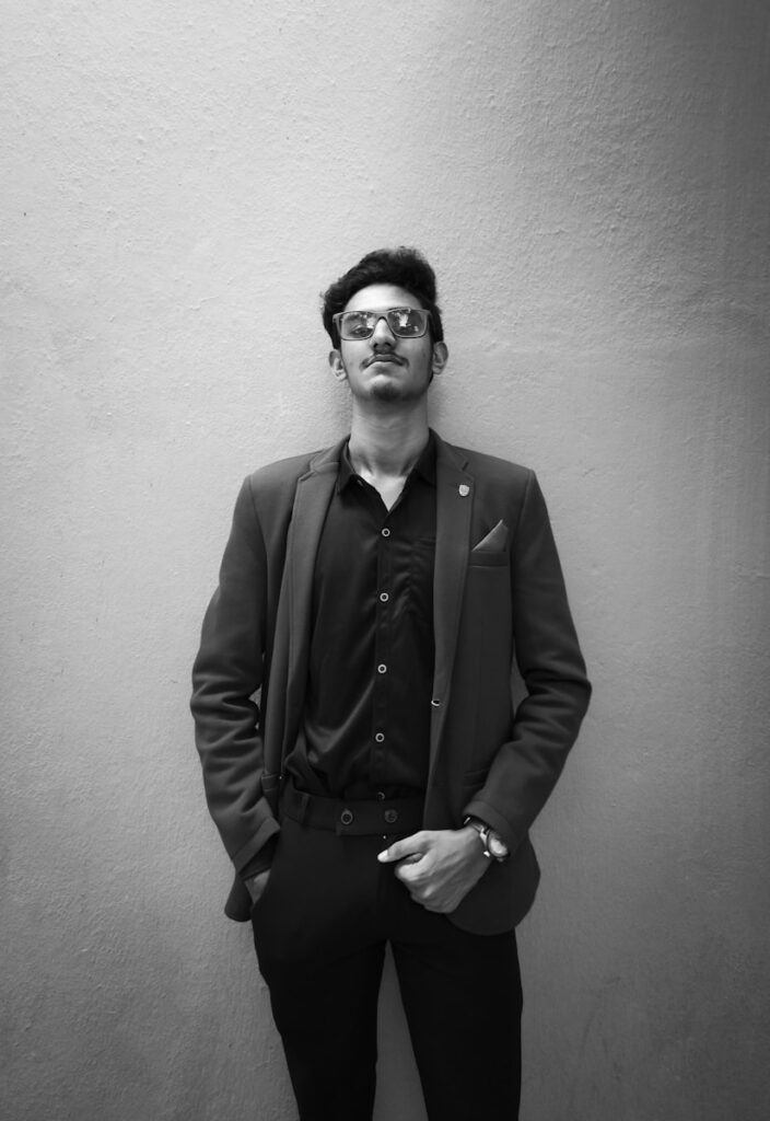 a man in a suit and glasses leaning against a wall
