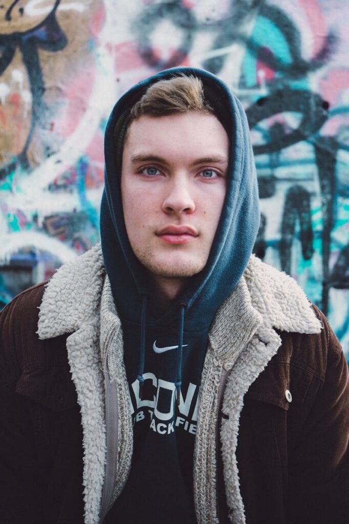Stylish young man in hoodie and jacket against graffiti backdrop. Urban fashion portrait.