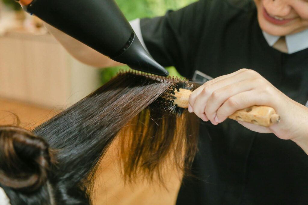 Close-up of hair stylist using a hairdryer and brush to style long hair.