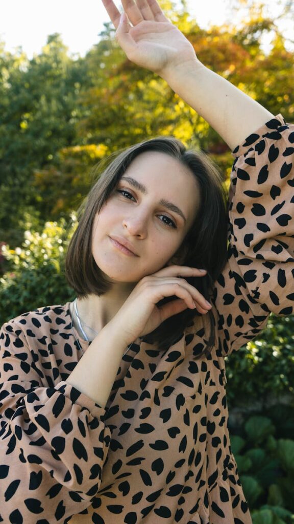 A young woman with a patterned top poses gracefully against a lush outdoor backdrop, showcasing natural beauty and charm.