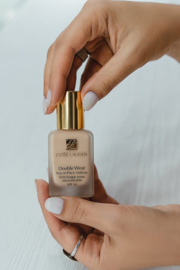 Close-up of hands holding a bottle of liquid foundation makeup on a white background.