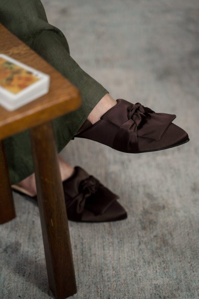 Close-up of brown satin mules worn indoors, providing a stylish and relaxed appearance.