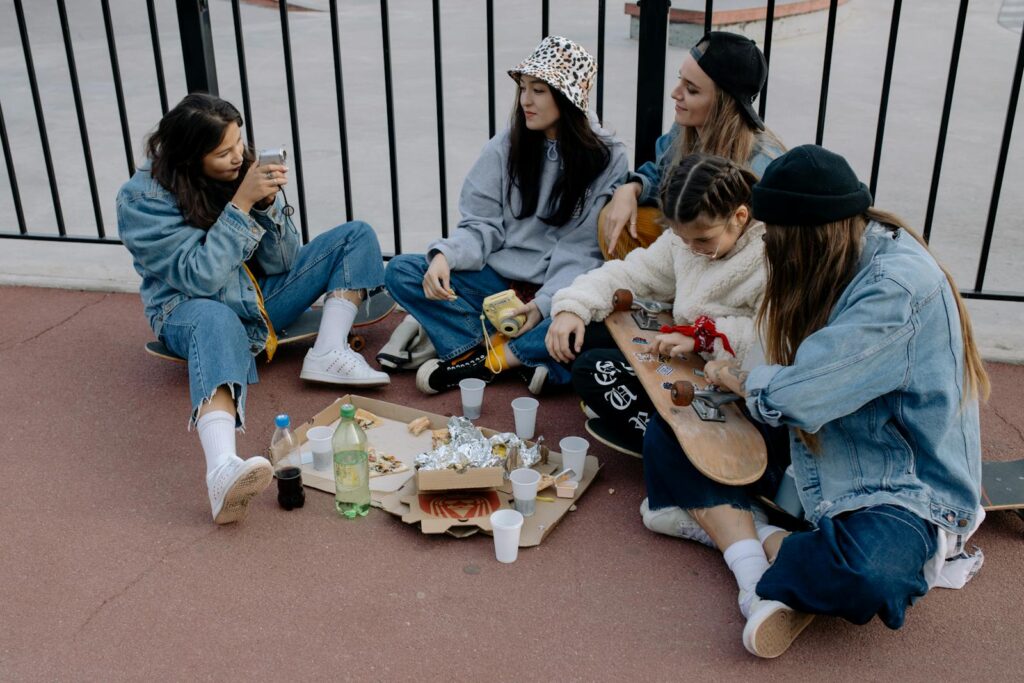Five friends gather outdoors sharing food and taking photos, enjoying each other's company.