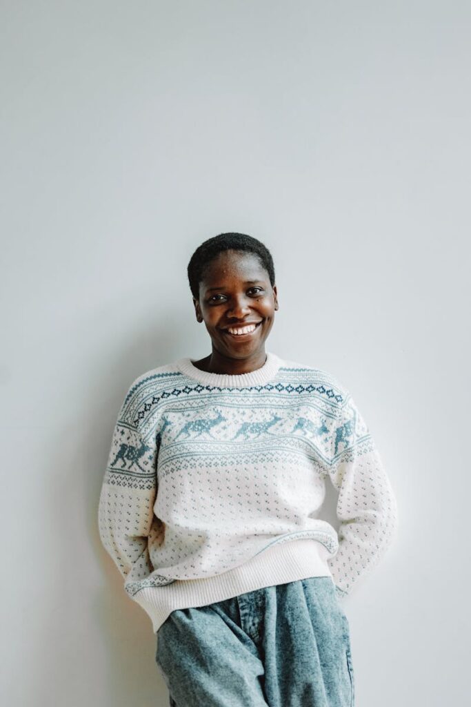 A cheerful woman in a Christmas sweater poses against a plain backdrop, radiating joy and warmth.