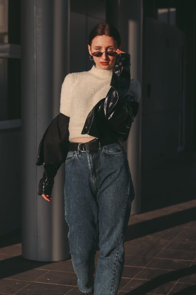 Stylish woman wearing sunglasses, oversized jacket, and jeans walking with confidence on a city street.