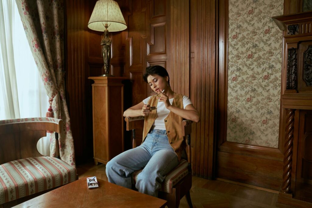 Woman sitting in a vintage living room, lighting a cigarette, calm and pensive mood.
