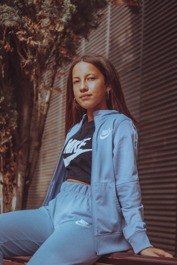 Teen girl wearing a Nike tracksuit and loop earrings sits confidently outdoors.