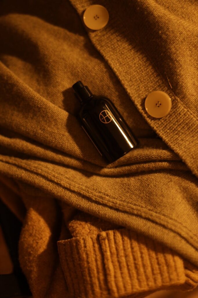 Black perfume bottle on soft knitwear with earthy tones in warm lighting.