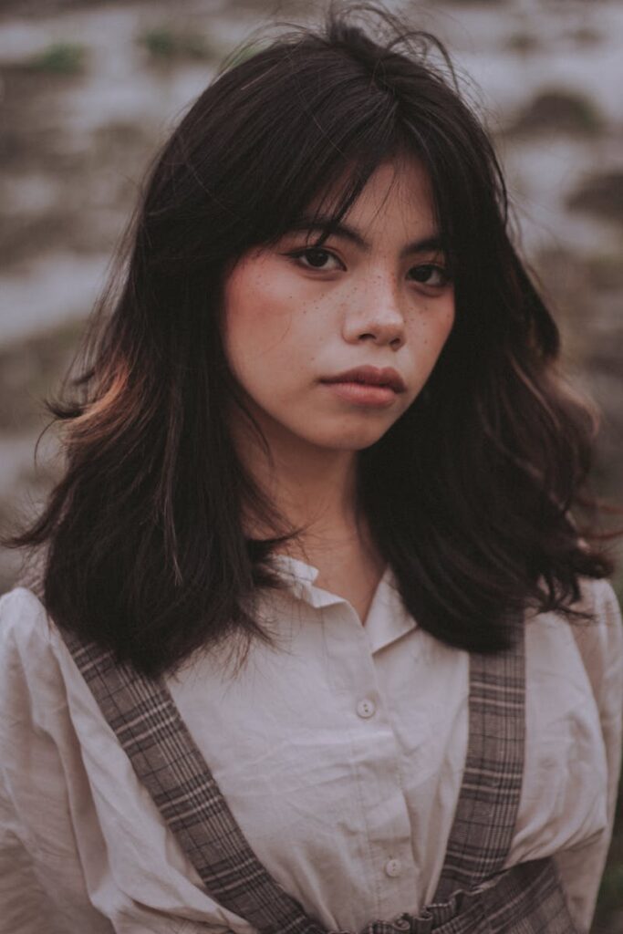 Close-up portrait of a woman with freckles and dark hair in soft outdoor lighting.