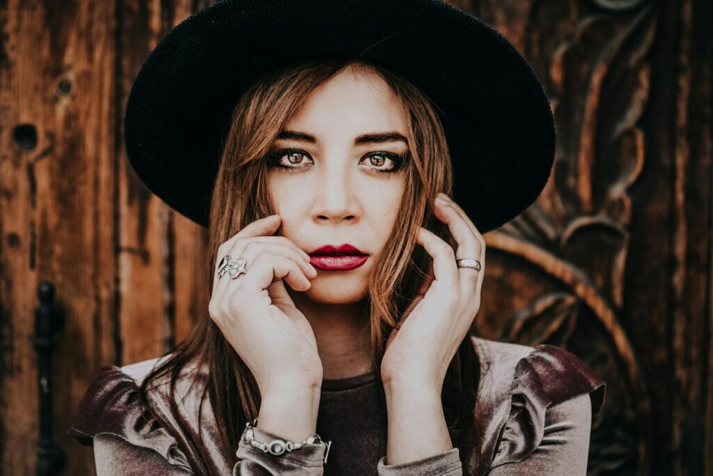 Fashionable woman wearing a hat poses against a wooden backdrop. Elegant and stylish look.