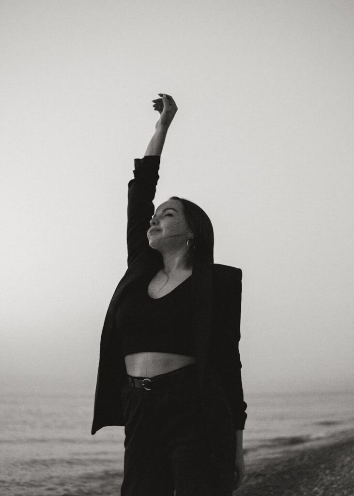 Artistic black and white photograph of a woman raising her hand at the beach, exuding a sense of freedom.