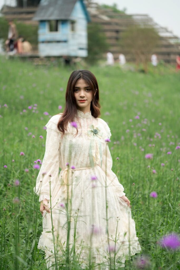 A woman in a vintage dress standing amidst a blooming meadow creating a serene and stylish portrait.