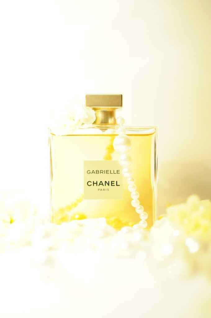 Elegant Chanel Gabrielle perfume bottle draped with pearls, glowing in a bright ambiance.
