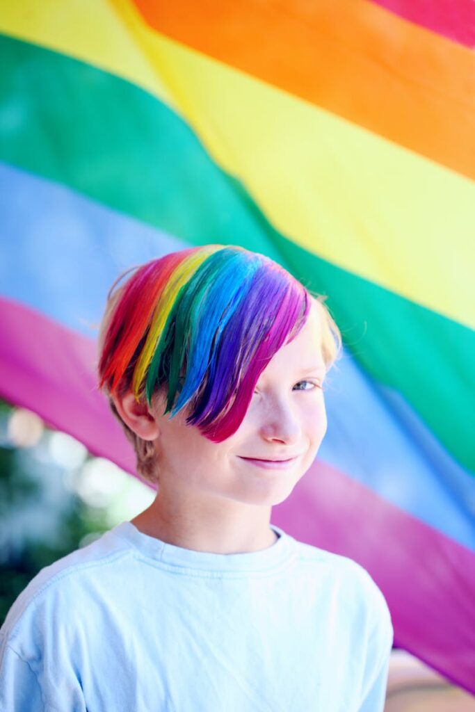 A joyful child with rainbow hair against a vibrant pride flag backdrop.