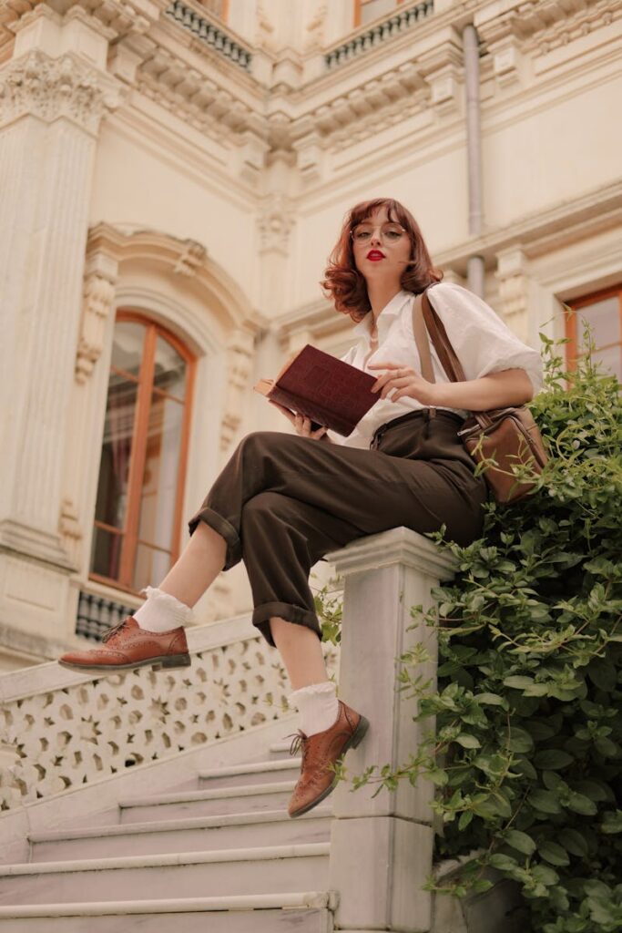 Stylish woman in vintage attire reading a book on ornate steps.