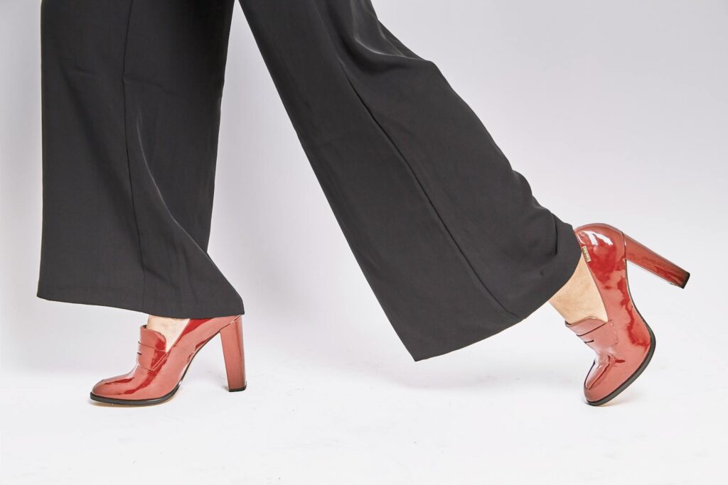 Stylish red high heels paired with black pants on a clean white background.