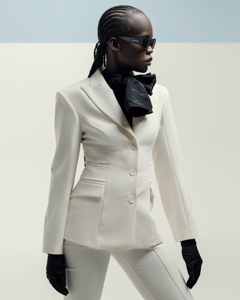 Stylish woman posing in a white suit with black accessories, showcasing elegance and fashion.