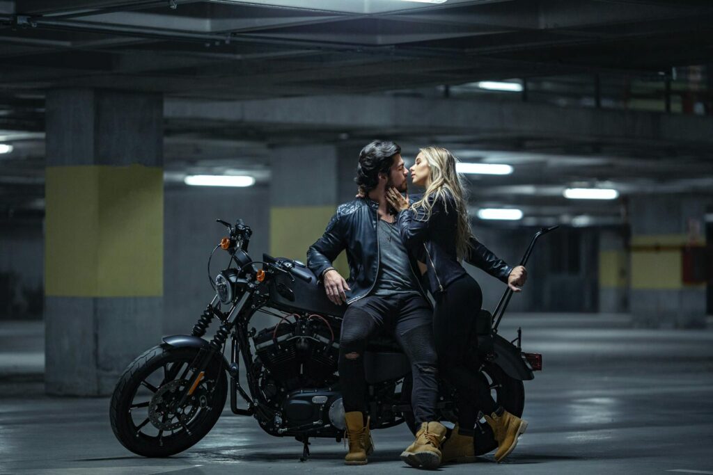 A couple embraces on a motorcycle in an underground parking garage, evoking a sense of adventure.