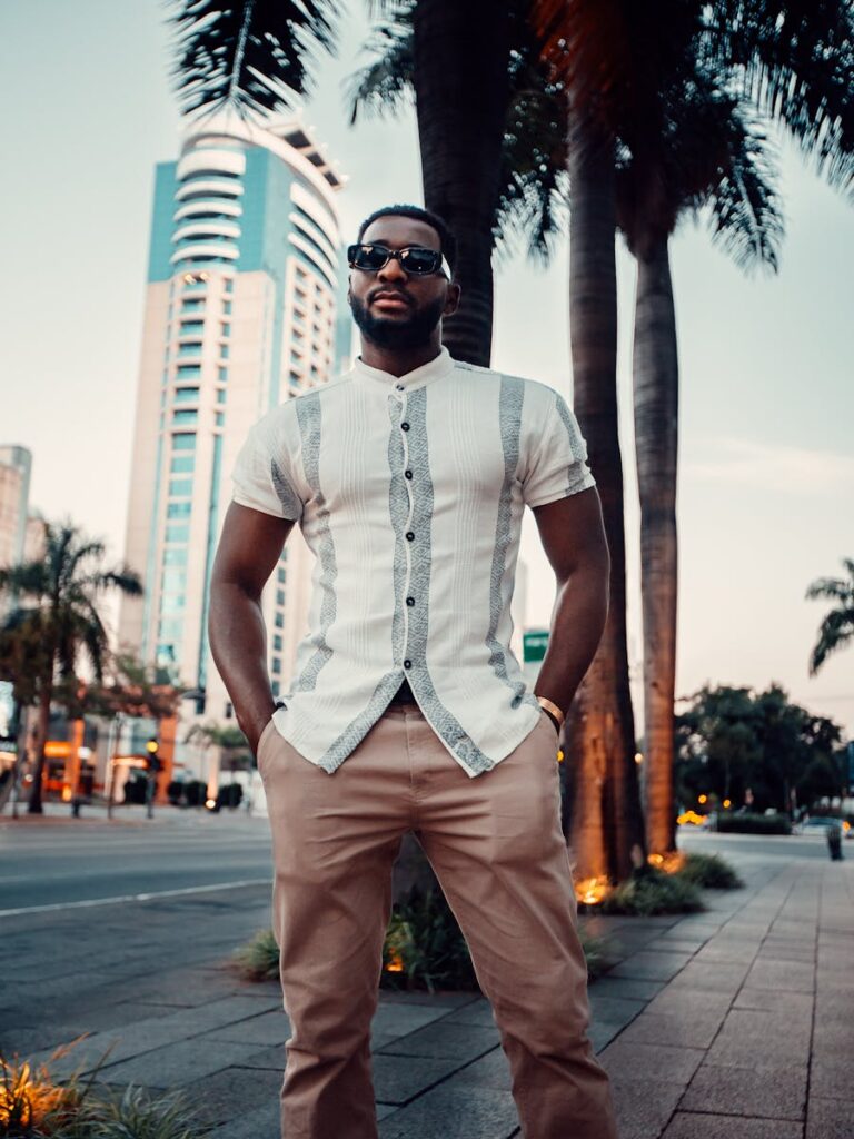 Fashionable adult man with sunglasses standing in city, exuding confidence amidst skyscrapers.