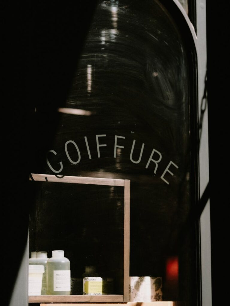 Moody shot of a coiffure shop's window reflecting hair products, emphasizing vintage storefront vibes.