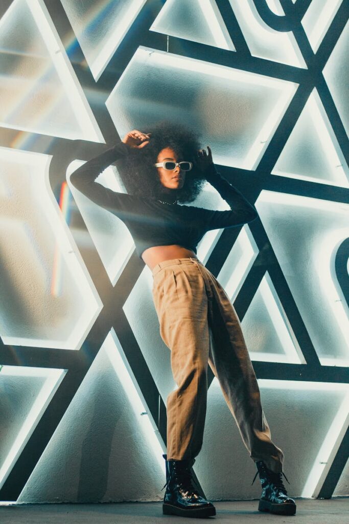Stylish woman in sunglasses leans against a geometric neon wall art.