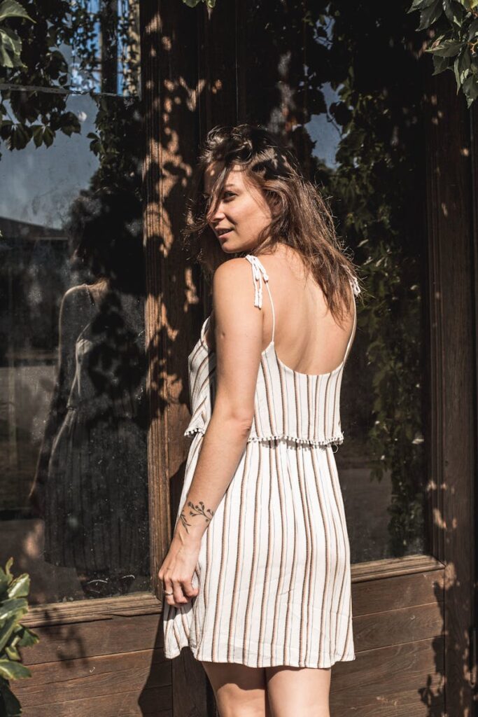 Woman in striped sundress enjoys sunlight while looking over shoulder outdoors.