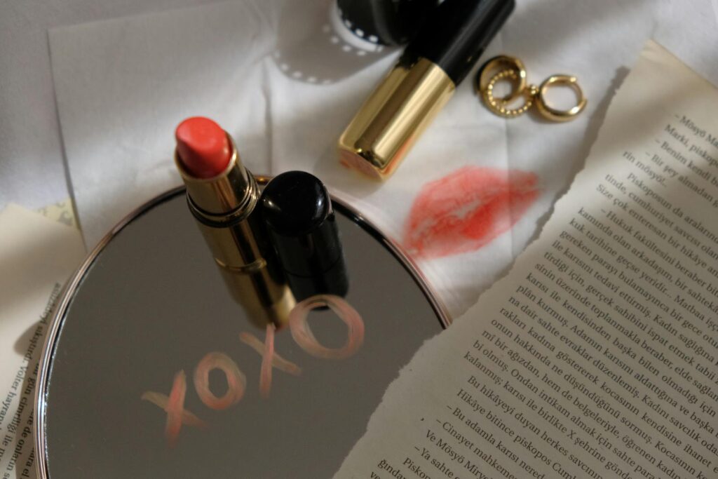 Stylish still life featuring lipsticks, gold earrings, and a mirror with a written message.