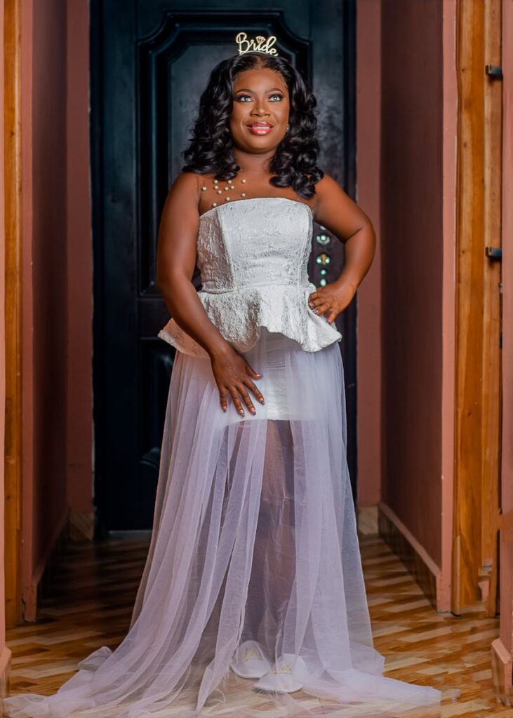 Portrait of a smiling bride in an elegant white wedding dress standing indoors.