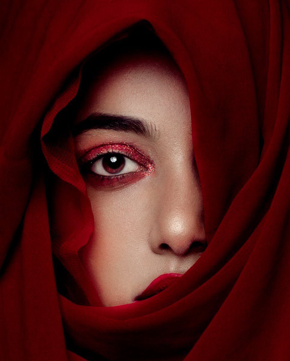 Close-up portrait of a woman's face partially covered by a flowing red veil, exuding mystery.