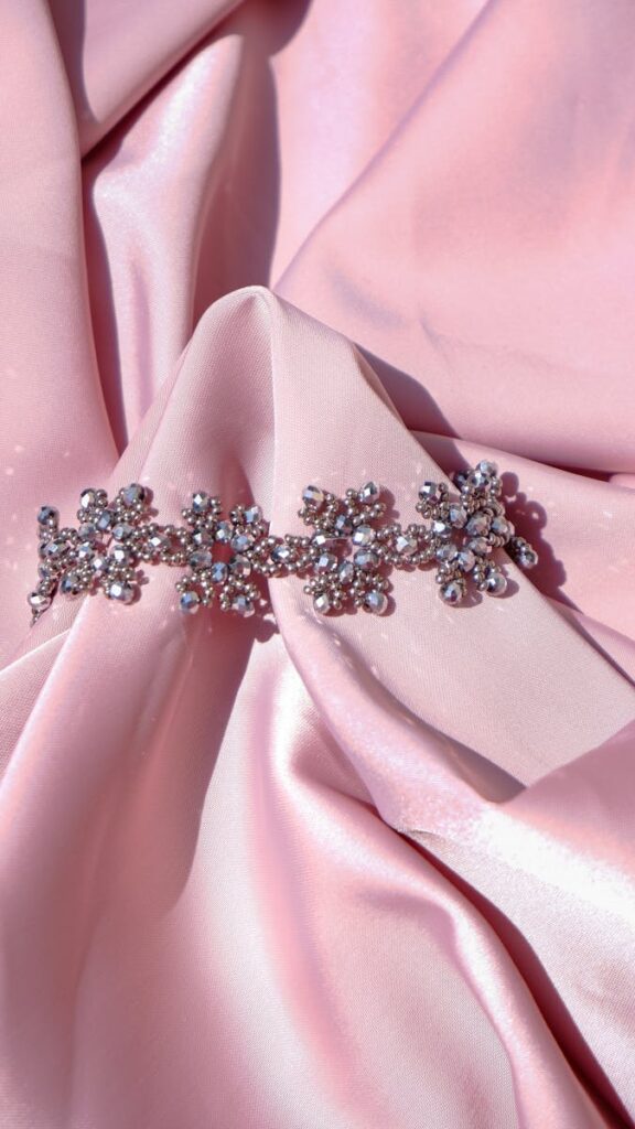 Close-up of a sparkling beaded bracelet on a soft pink satin background, perfect for fashion and accessory themes.