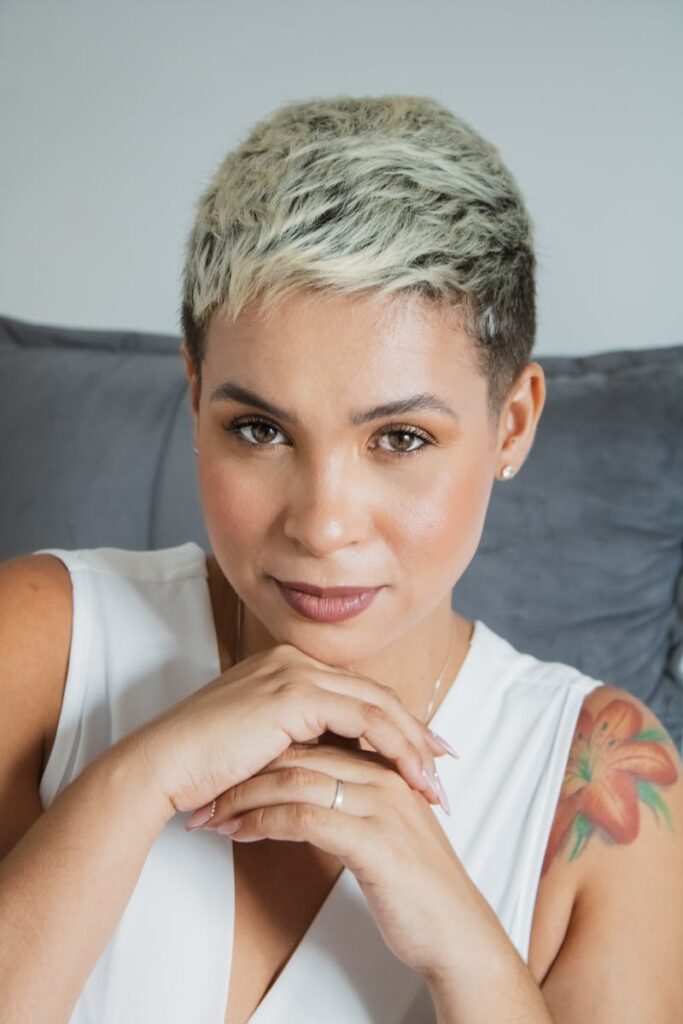 Portrait of a smiling woman with a pixie cut and floral tattoo in a casual setting.