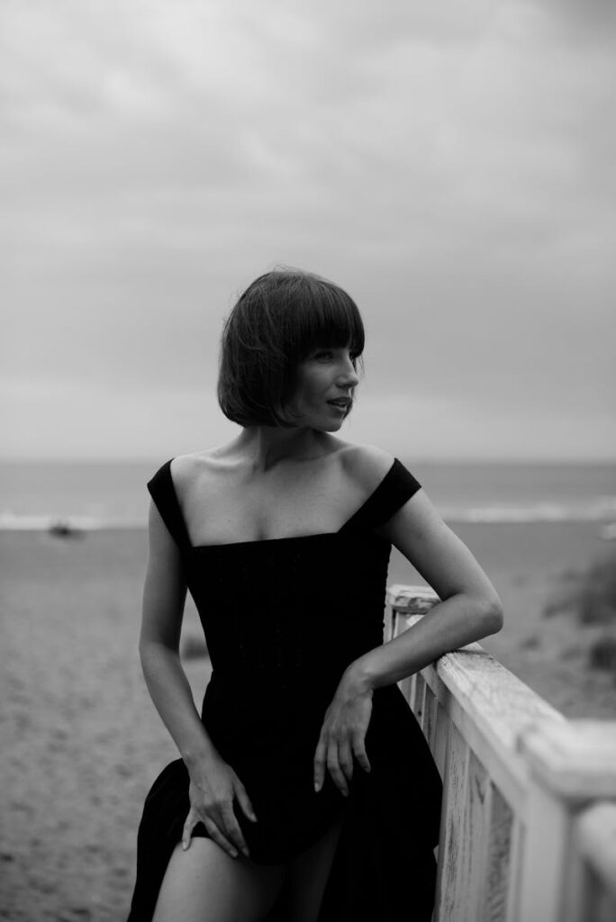 Black and white portrait of a woman in a dress by the ocean shore.