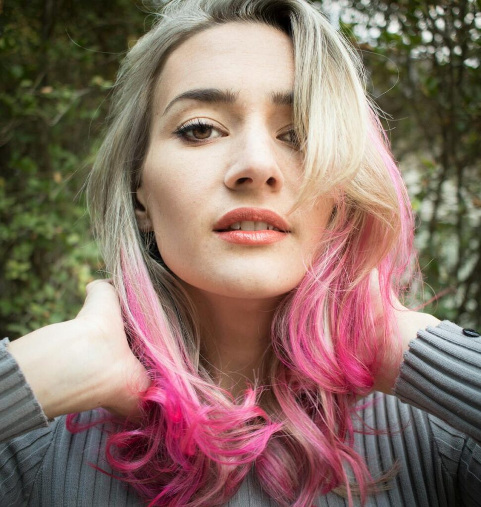 Close-up portrait of a young woman with pink hair in an outdoor setting, exuding a fashionable and confident look.
