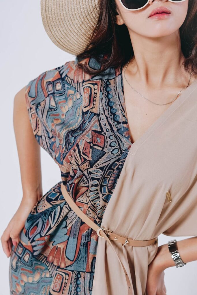 Stylish woman in a bohemian dress and straw hat posing against a gray background.