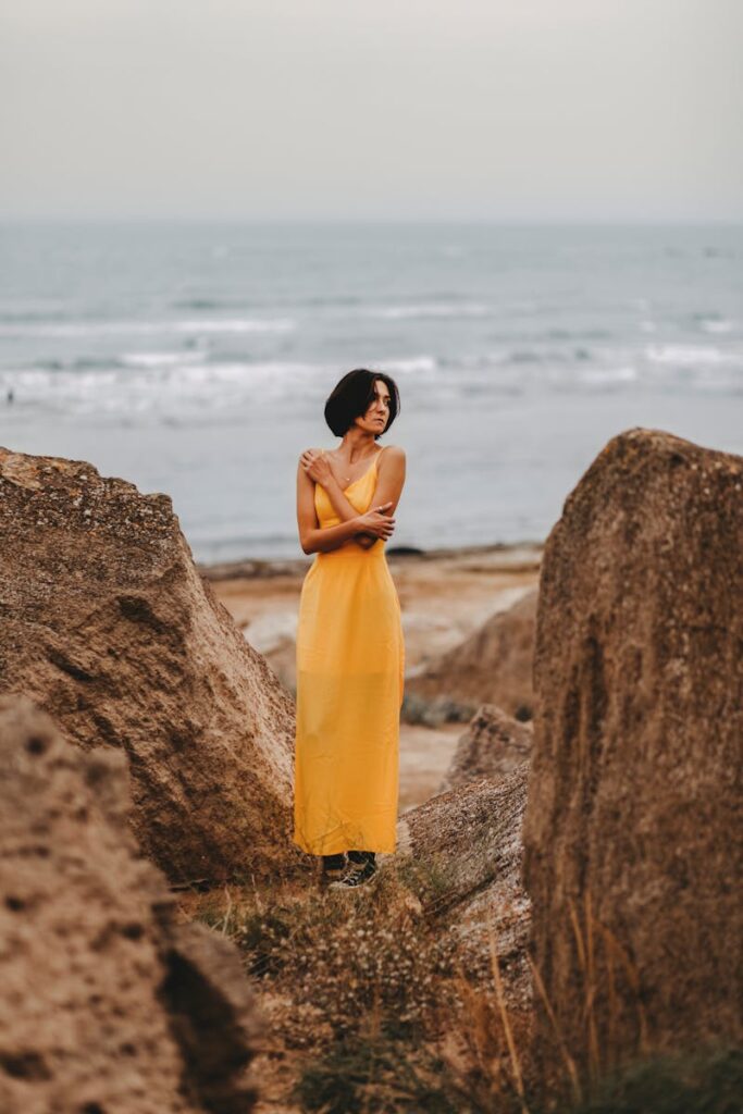 Woman in a yellow dress posing among rocks by the sea in Baku, Azerbaijan.