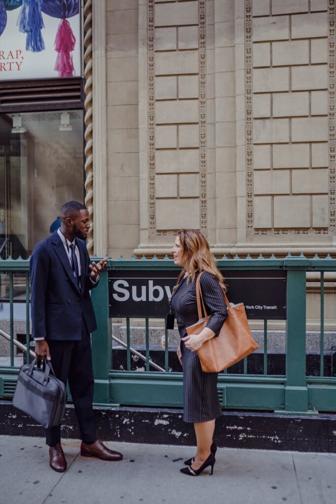 Businessman and businesswoman conversing outside a subway entrance on a city street.