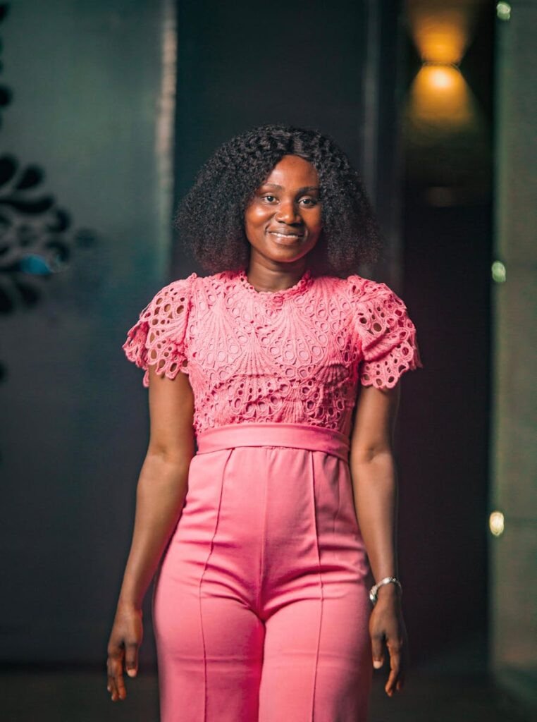 A woman posing indoors in a stylish pink lace blouse and high-waisted pants, showcasing fashion elegance.