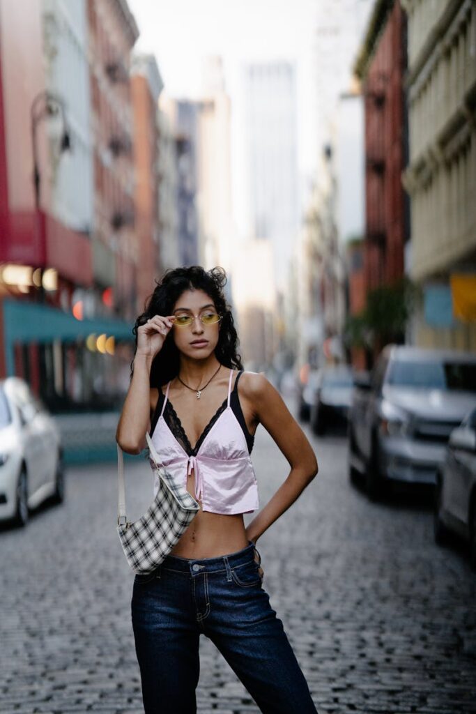 A young woman poses stylishly on a city street wearing a crop top and jeans, highlighting urban fashion.