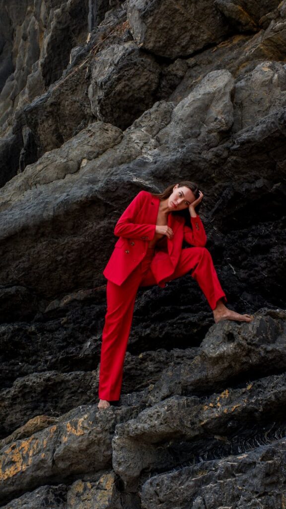 Elegant woman wearing red suit poses confidently against dramatic rock formations.
