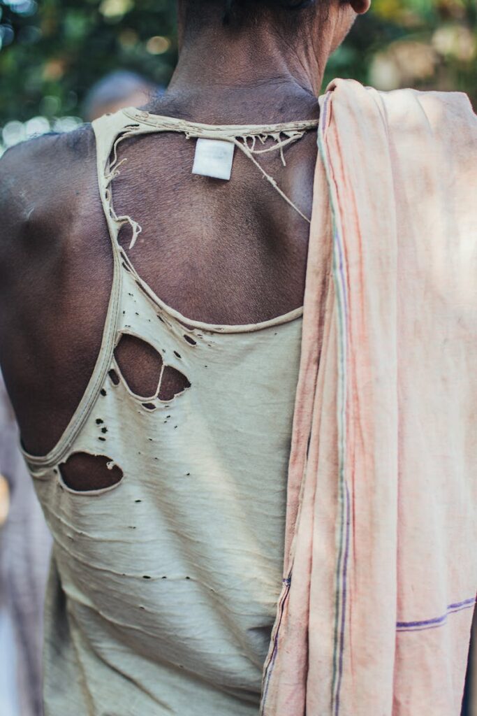 A close-up of a man wearing a torn shirt outdoors, captured from behind.