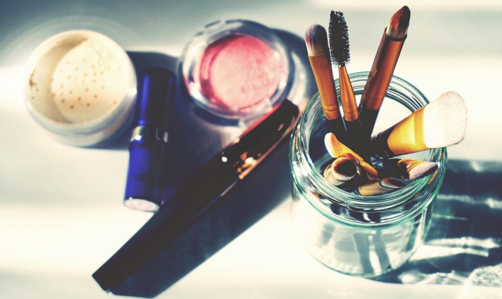 Artistic flat lay of makeup brushes in a jar surrounded by colorful cosmetics, perfect for beauty themes.