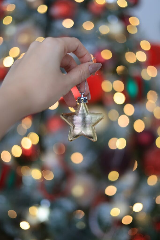 Close-up of a hand holding a golden star ornament in front of a bokeh-lit Christmas tree.