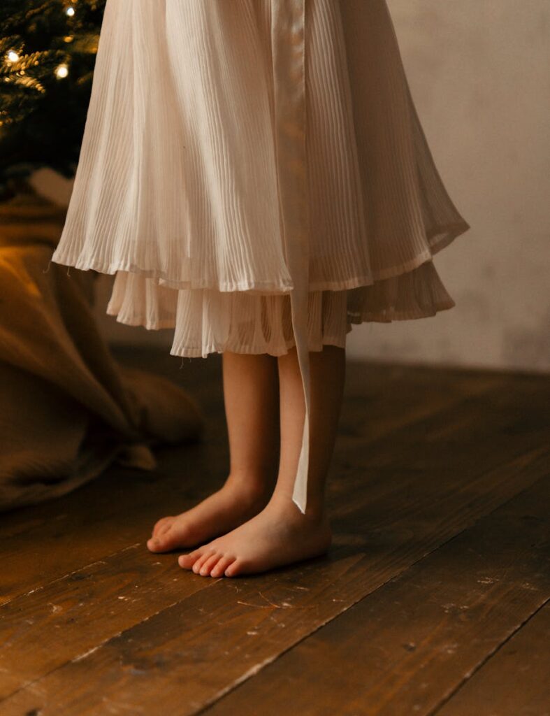 Delicate image of a barefoot child in an ivory dress on wooden floor, perfect for serene themes.