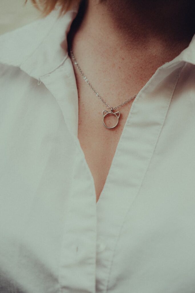 Close-up of an elegant silver cat pendant necklace on a classic white blouse.