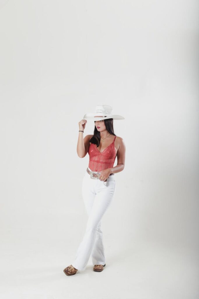 Elegant woman in a studio wearing trendy fashion with a hat and white jeans.