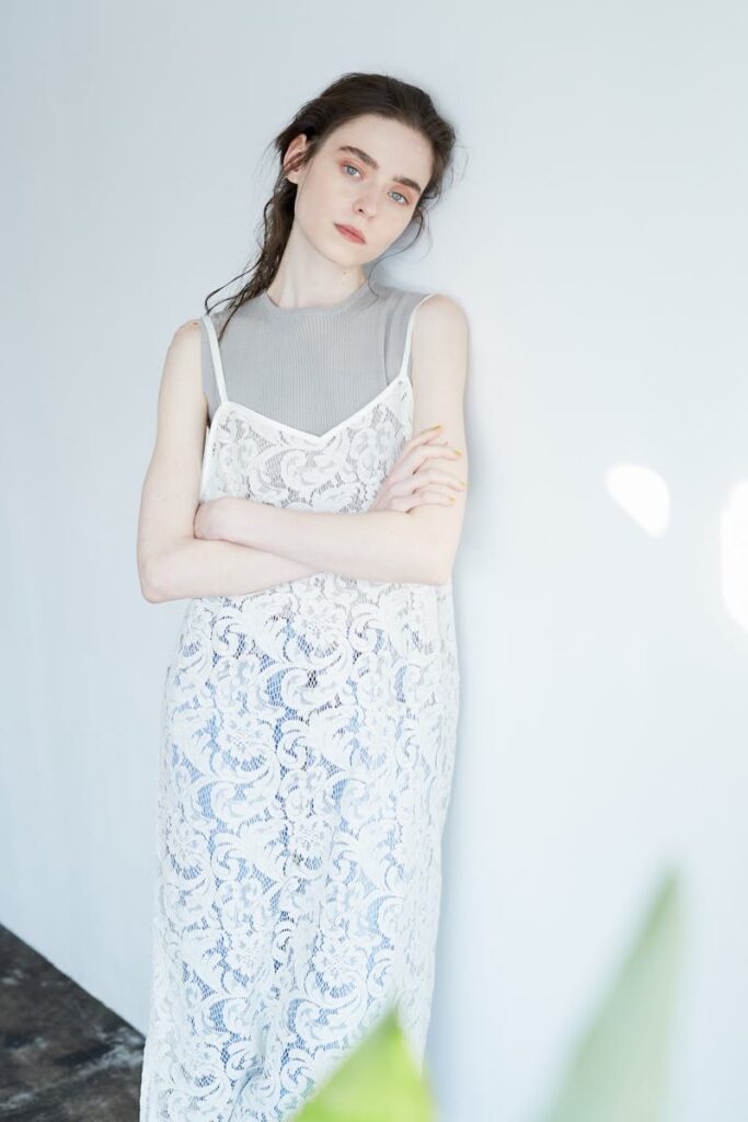 Graceful woman in a white lace dress poses with arms crossed in a bright indoor setting.