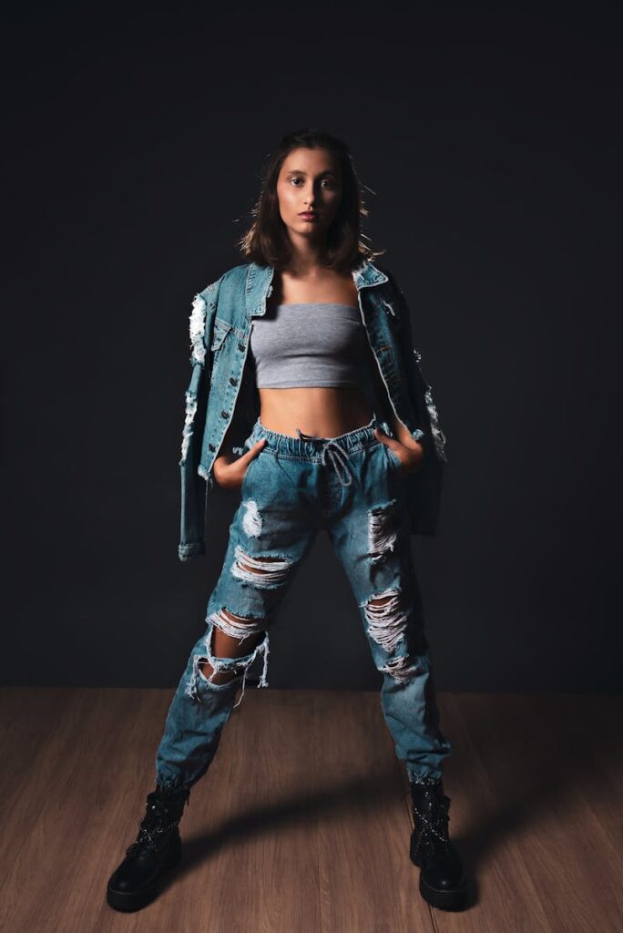 Woman in stylish distressed denim jacket and jeans, posing confidently indoors.