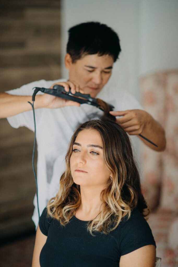 Hairdresser using curling iron on woman's wavy hair in salon.