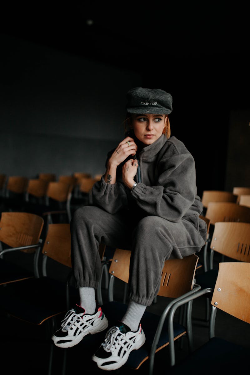 A woman in casual grey attire sits pensively on a chair in a dimly lit auditorium.